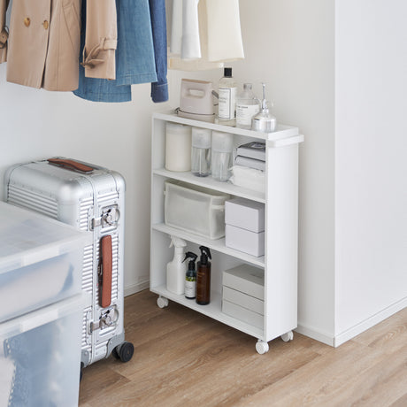 Hvit oppbevaringsvogn på hjul plassert ved seng på soverom.