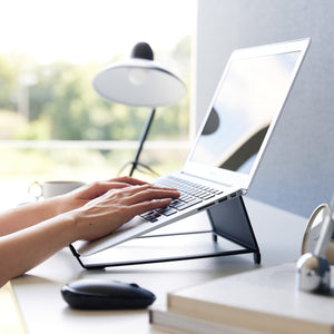 Justerbart stativ i sort metall med nettbrett plassert på kontorpult.