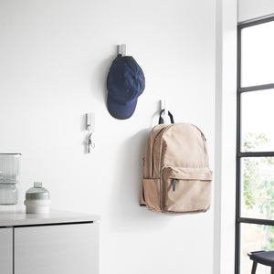 Praktiske hvite kroker montert på vegg med vesker og ryggsekk hengende.