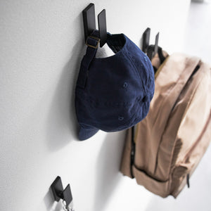 Sorte veggkroker i metall plassert i gang med hatt, jakke og veske.