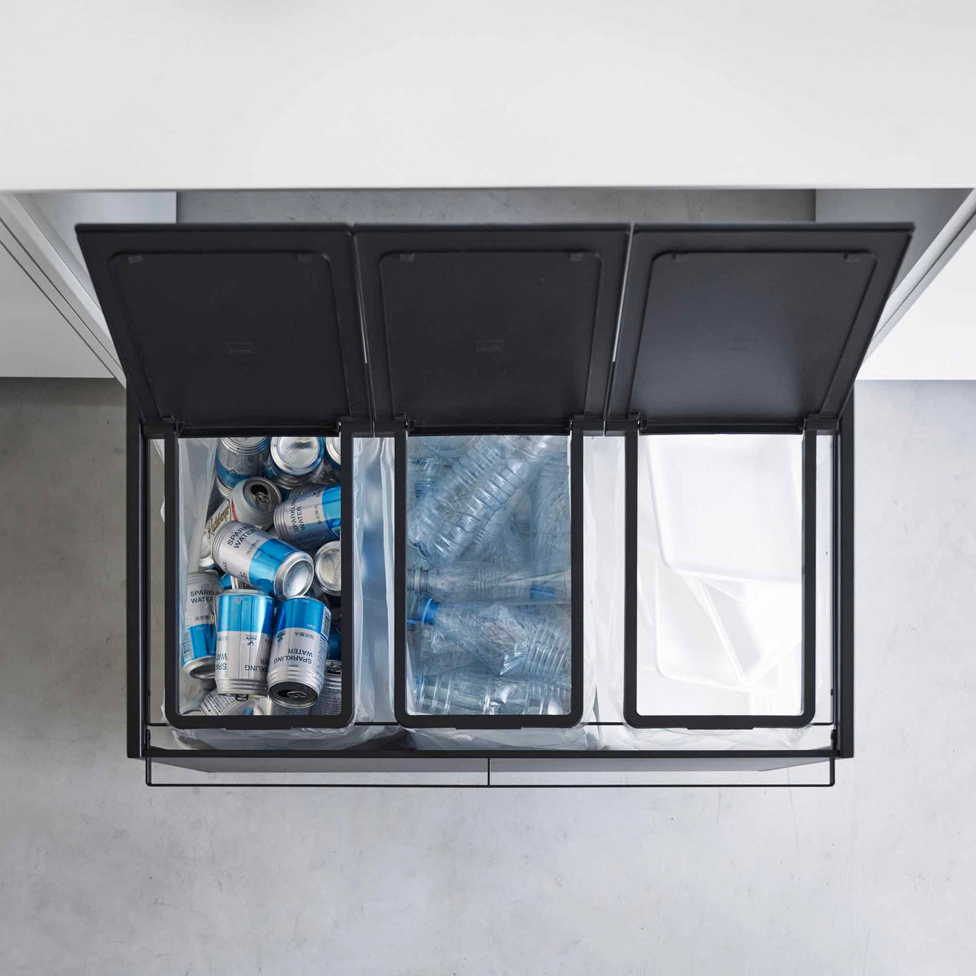 Kildesorteringsstativ med tre rom og åpne lokk som viser sortering av flasker og plast