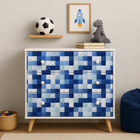 Hvit kommode med blå LEGO-foliedesign på skuffer, stylet med leker og bøker.