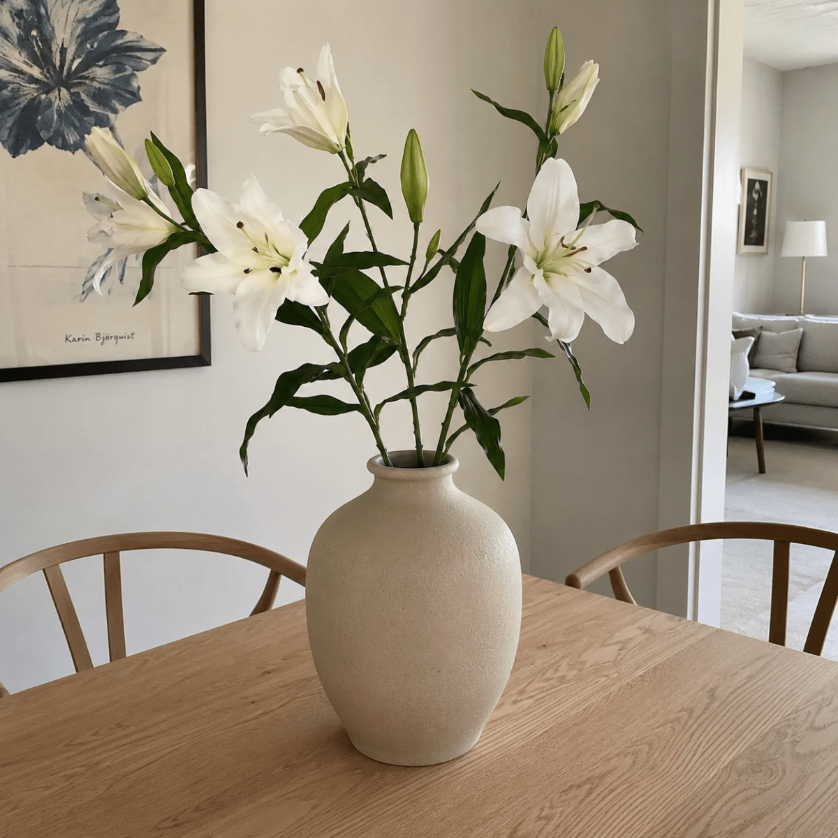 Kunstig hvit lilje med realistiske blomster og blader på grønn stilk. I kraftig keramikkvase i et nordisk hjem
