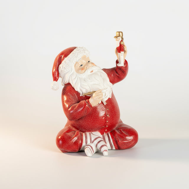 Dekorativ nissefigur i rød drakt, sittende med en liten gullfigur i hånden.
