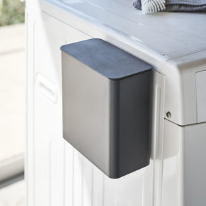 Sort magnetisk oppbevaringsboks festet på vaskemaskin.