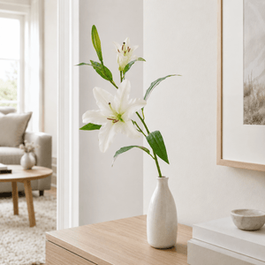 Kunstig hvit lilje med realistiske blomster og blader på grønn stilk. I hvit keramikkvase i et nordisk hjem