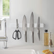 Magnetisk hvit knivholder montert på kjøkkenvegg med kniver og sak.