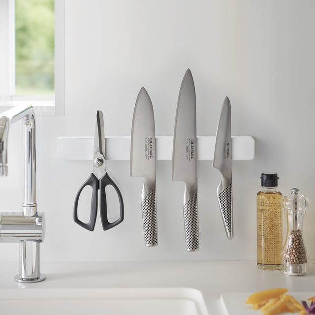 Magnetisk hvit knivholder montert på kjøkkenvegg med kniver og sak.