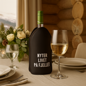 Vinkjøler med "Nyter livet på fjellet"-tekst på festpyntet bord i fjellhytte, med vin og blomsterdekorasjon.