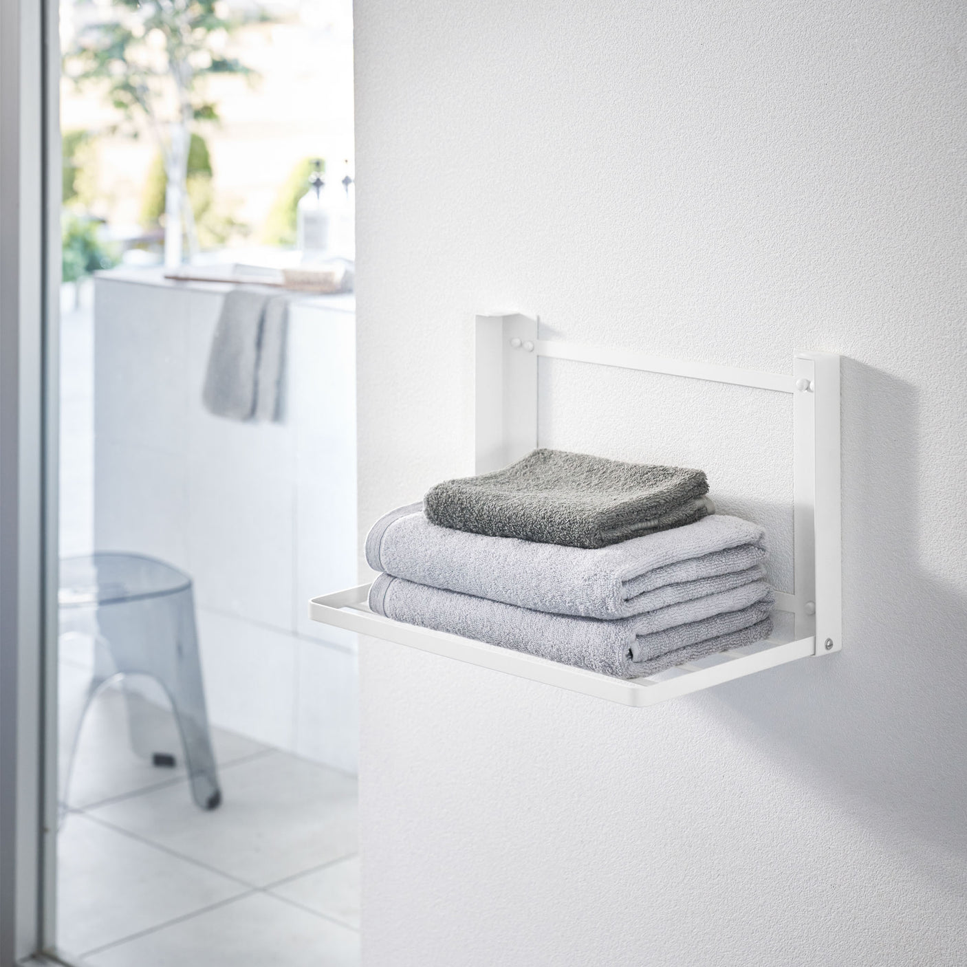 Hvit sammenleggbar vegghylle montert på bad med håndklær.