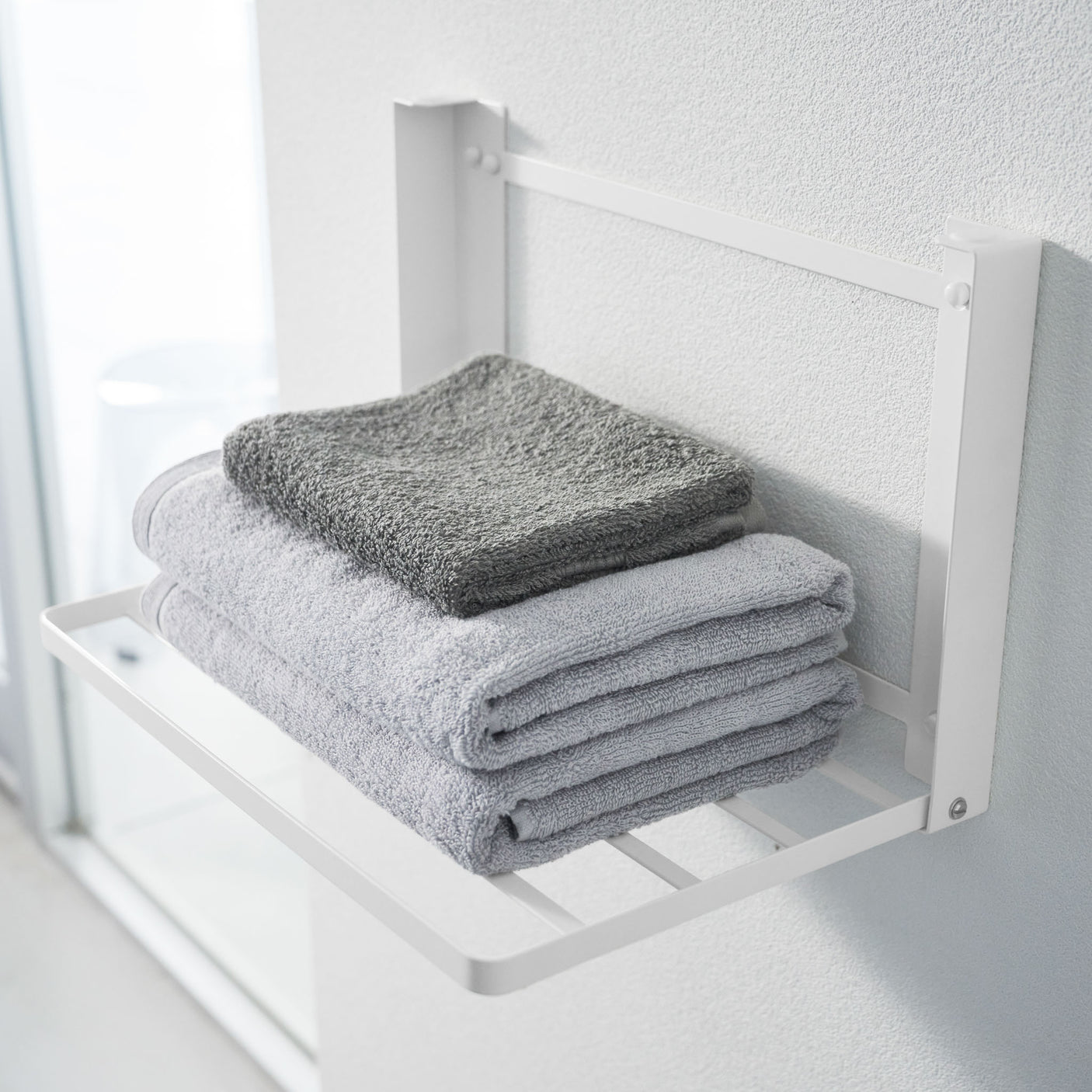 Minimalistisk vegghylle i hvit farge montert over håndklestativ.