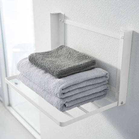 Minimalistisk vegghylle i hvit farge montert over håndklestativ.