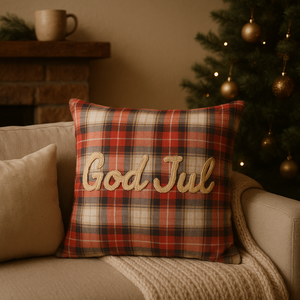 "Putetrekk i rødt rutemønster med teksten God Jul, plassert i beige sofa med juletre i bakgrunnen – klassisk julepynt til stue.