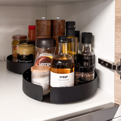 Sort roterende brett med høy kant holder glass og flasker organisert og tilgjengelig – smart løsning for effektiv oppbevaring i kjøkkenskap.