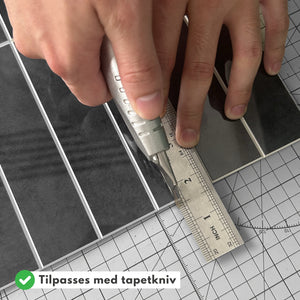 Hender som kutter Alma antrasitt marmorfliser med tapetkniv.