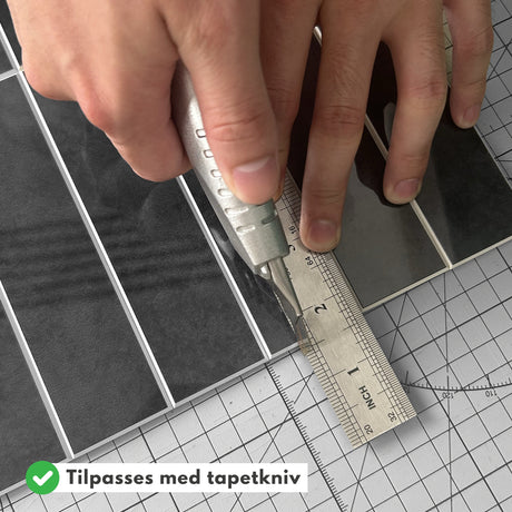 Hender som kutter Alma antrasitt marmorfliser med tapetkniv.