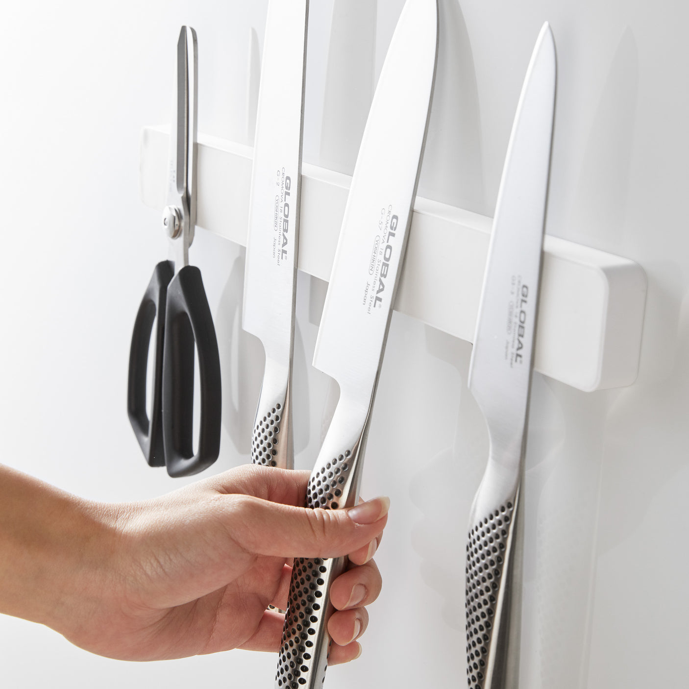 Hånd som setter kniv på hvit magnetisk knivholder.