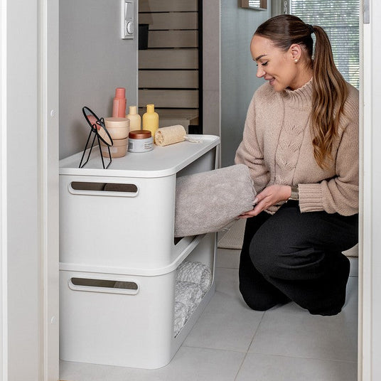 1. Kvinne som organiserer stablede hvite oppbevaringsbokser i garderobe