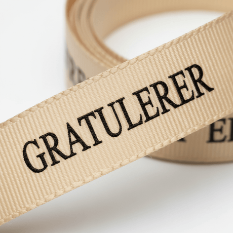 Beige pyntebånd med sort tekst for dekorative gaver