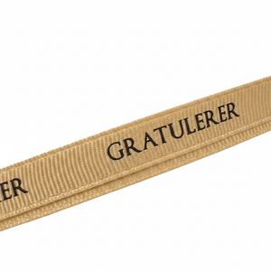 Nærbilde av beige grosgrainbånd med sort «Gratulerer»-tekst. - Lindas dekor