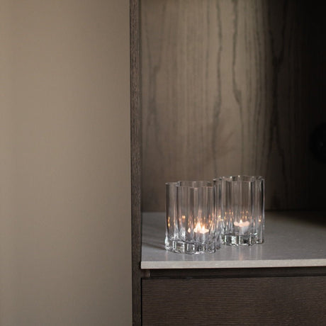 Flere klare lyslykter i rillet glass plassert på mørk hylle med elegant kontrast.