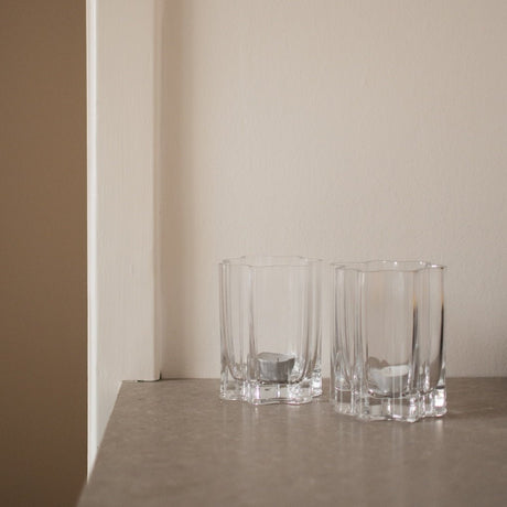 To klare lyslykter i rillet glass plassert på lys hylle i rolig og moderne interiør.