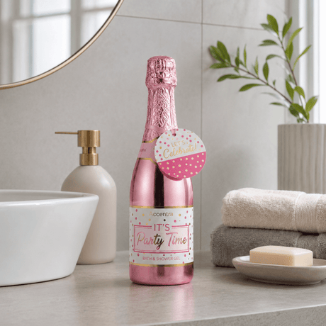 Rosa bade- og dusjsåpe i champagneflaske på baderomsbenk i lyst, nordisk baderom.