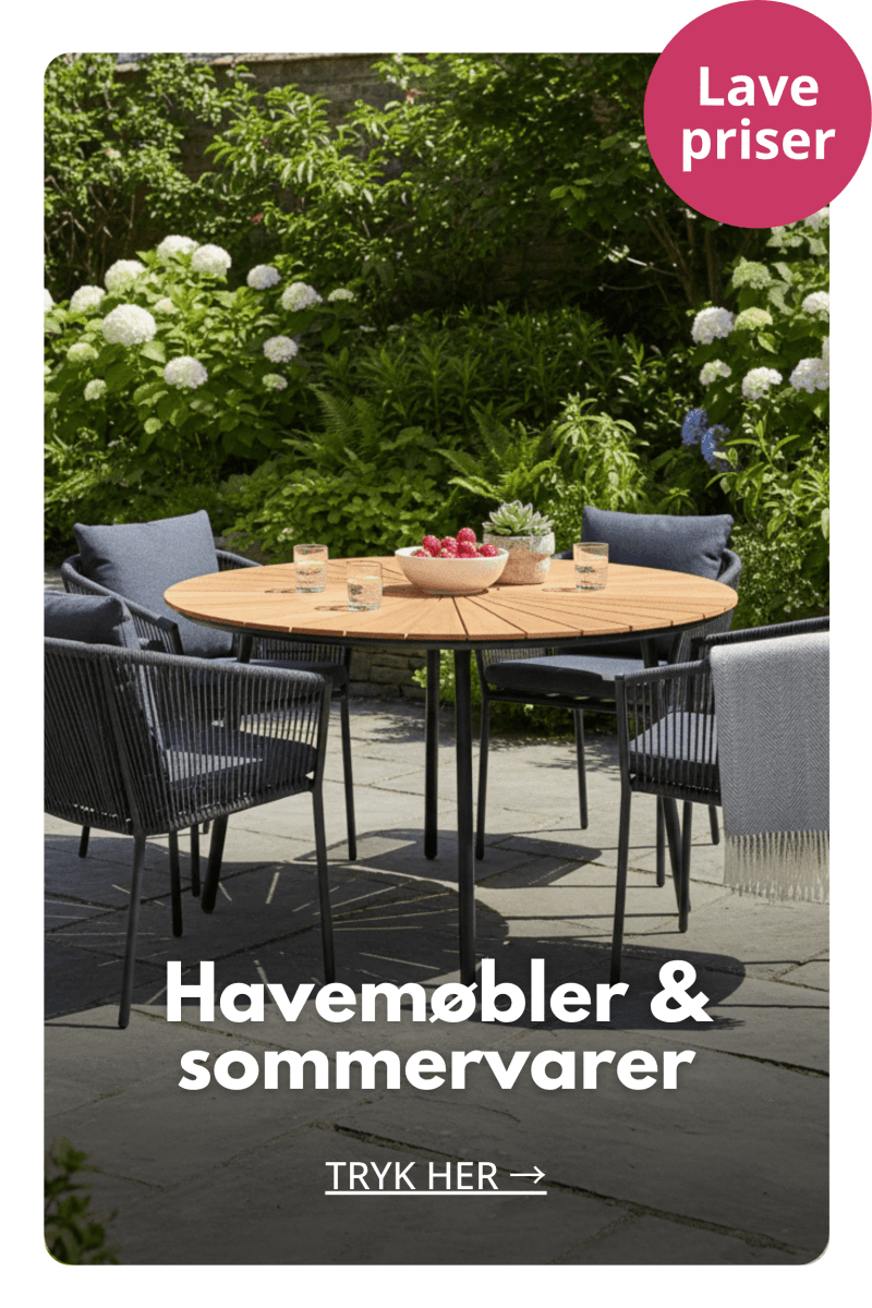 Rundt havebord med stole på terrasse omgivet af grønne planter og sommerblomster