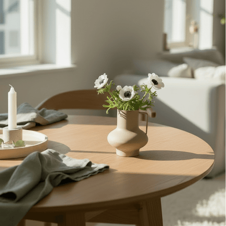 Matt sandfarget vase med hvite blomster på rundt trebord i nordisk stue