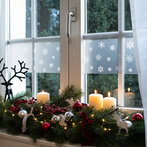 Snowflake vindusfolie med snøfnuggmønster på vindu med julepyntet vinduskarm med granbar, stearinlys, julekuler og lysdekorasjoner i varm julekos