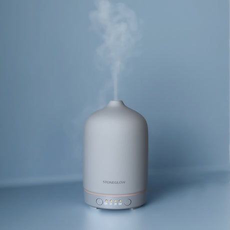 Aromadiffuser i matt grå keramikk med damp som stiger opp.