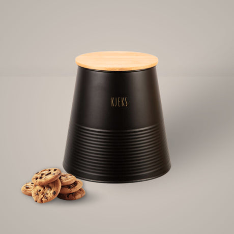Sort metallboks med bambuslokk og gulltekst «Kjeks», plassert på kjøkkenbenk med kjeks ved siden av.