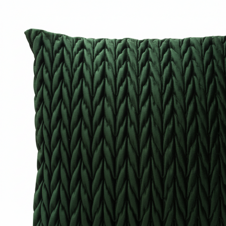 Flettet velur putetrekk i dyp flaskegrønn på lys sofa med dekor i bakgrunnen.