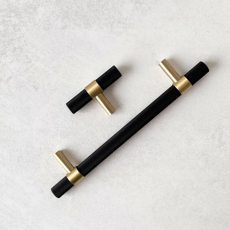 Kort og langt T-bar håndtak i sort og messing ligger på lys overflate.