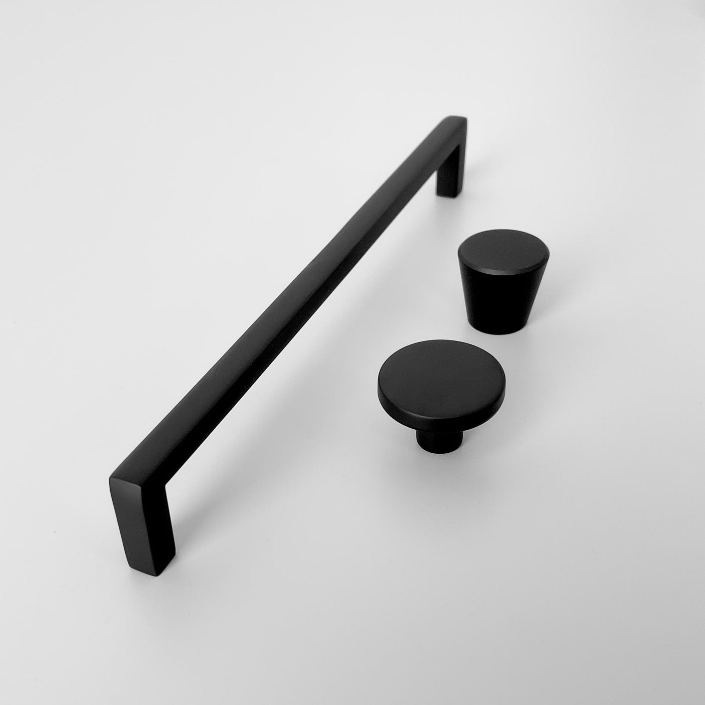 Sort matt knott og håndtak i moderne design, vist sammen med tilhørende knotter i samme stil, på hvit bakgrunn.
