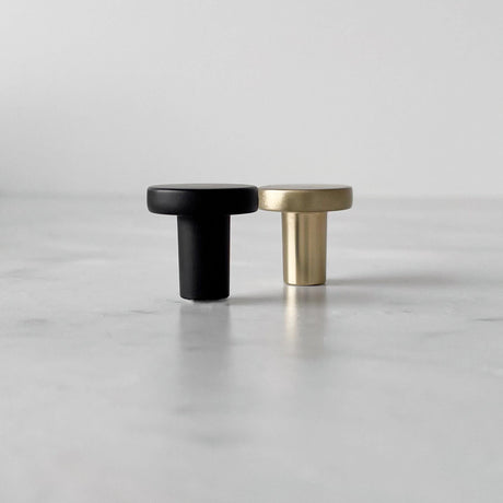 Moderne knotter i matt sort og messing vist sammen på lys overflate.