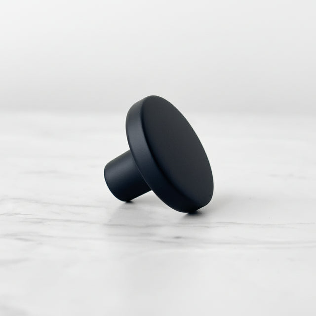 Sort matt knott med rund form og glatt overflate, fotografert liggende på en lys marmorinspirert bakgrunn.